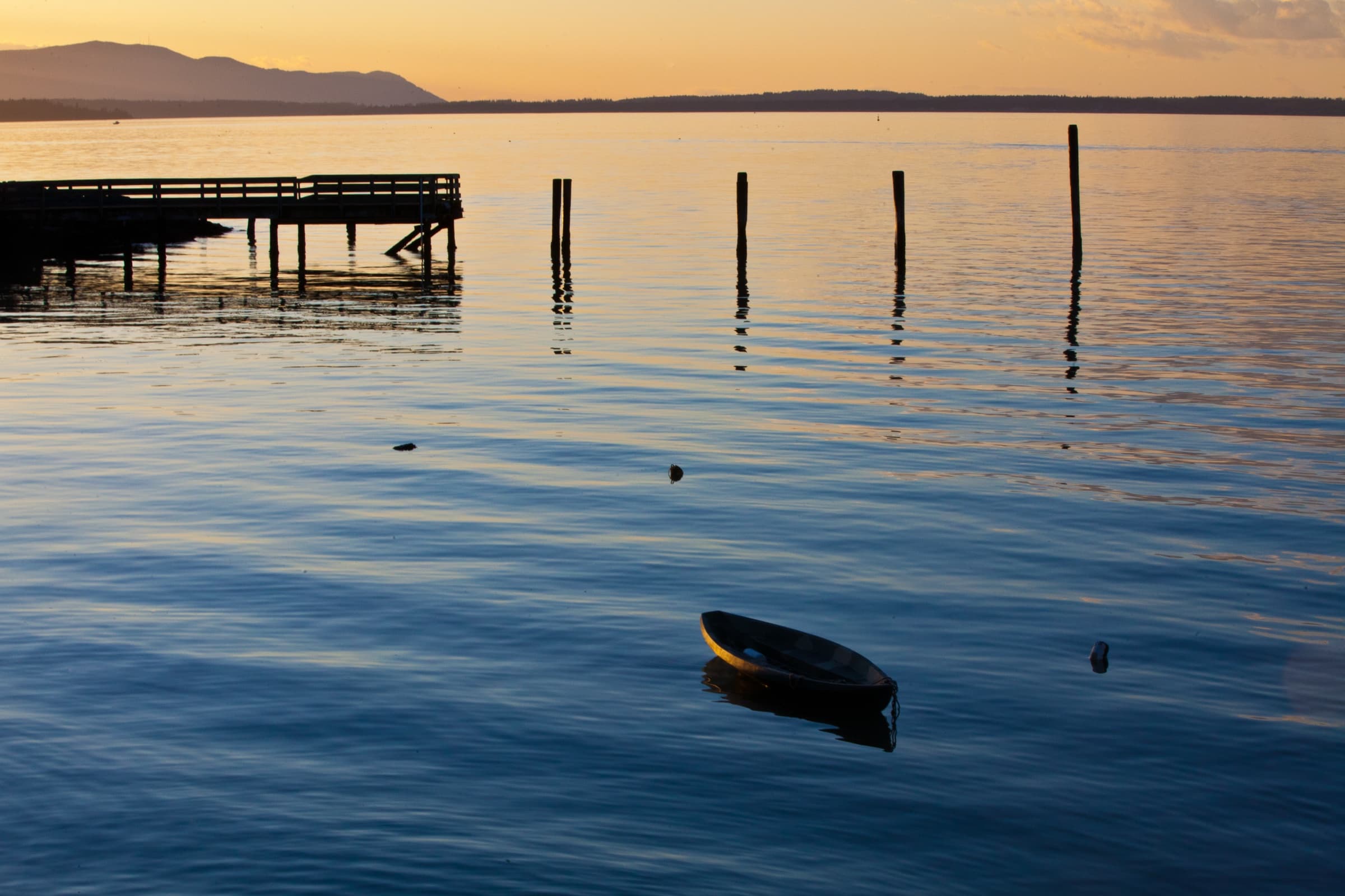 A lone boat resting on Bellingham Bay at dusk off Boulevard Park, a wooden pier silhouetted against the sunset