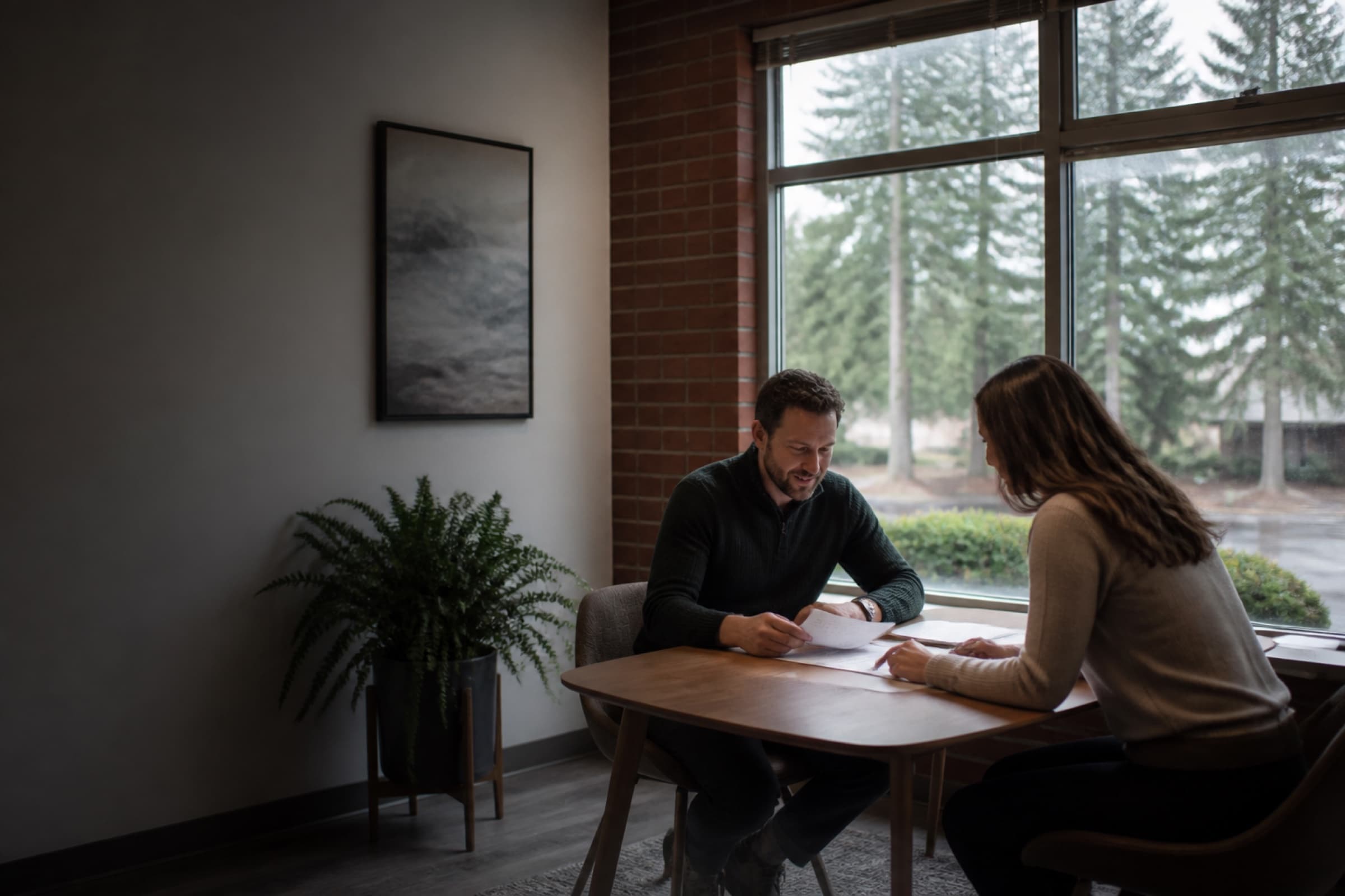 Two people reviewing papers in a light-filled commercial suite with cedar trees outside